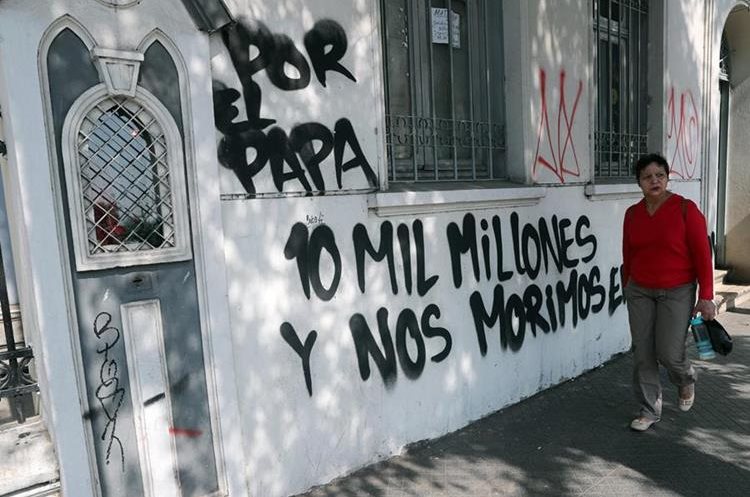 Una mujer camina frente a la Iglesia Cristo Pobre cuyas paredes frontales fueron rayadas con mensajes en contra de la visita papal en Santiago, Chile. (Foto Prensa Libre: EFE)