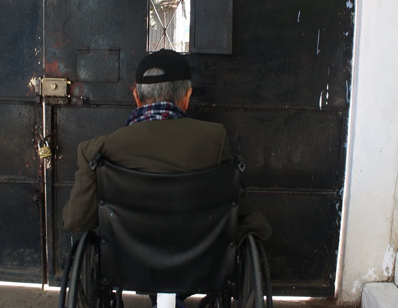 Carlos Enrique espera sentado en su silla de ruedas, quizás algún día, pueda comprar un billete a algún vendedor que pase por la calle.