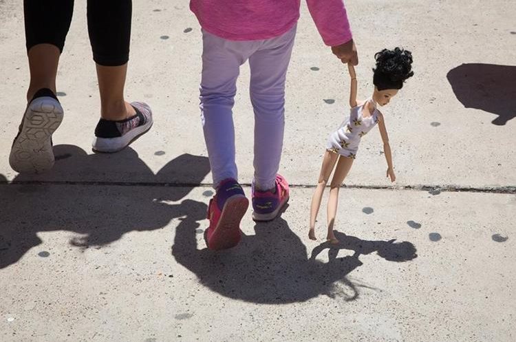 Una niña hondureña de 4 años carga una muñeca mientras camina con su madre inmigrante, ambas liberadas de un centro de socorro en McAllen. Texas. (AFP).