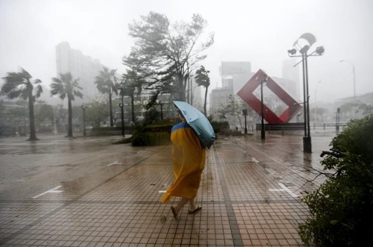 Un mujer se protege del viento y la lluvia  en Kaohsiung, Taiwán. (EFE).