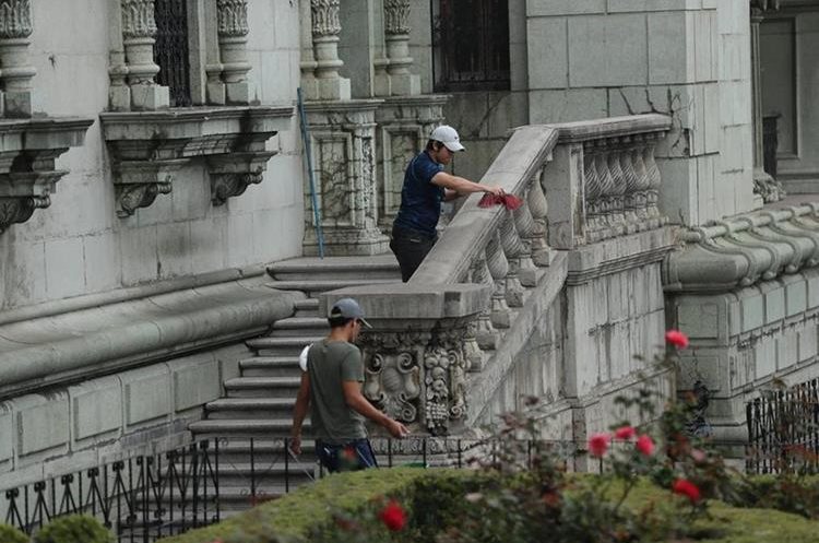 Trabajadores del Palacio Nacional de la Cultura sacuden la arena volcánica que quedó en el edificio. (Foto Prensa Libre: Esbin García)